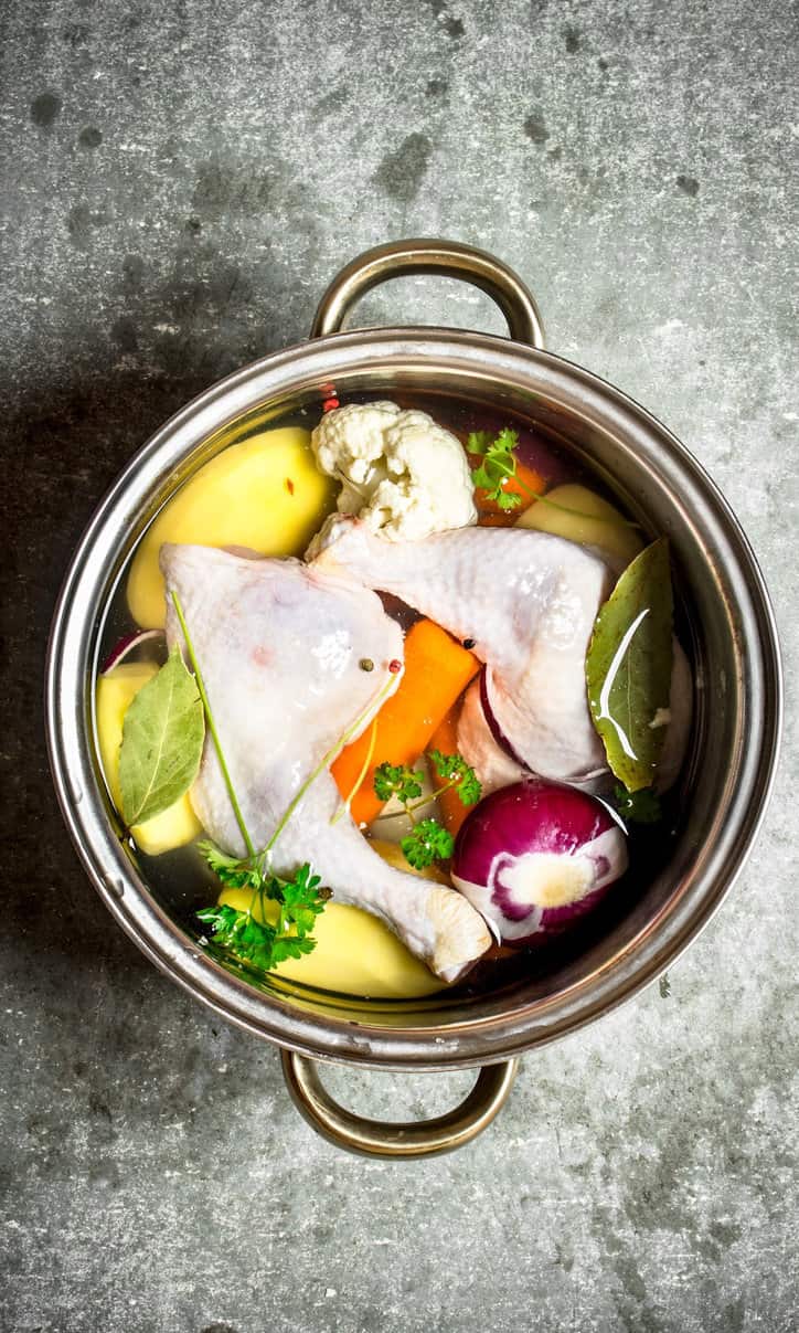 raw chicken, herbs, and vegetables in a pot with water