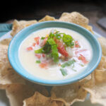 white cheese dip in a blue bowl with tomatoes and green onions on top