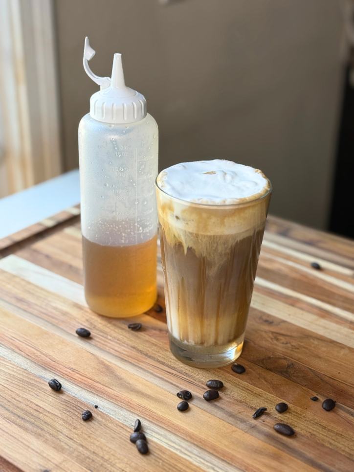 cup of iced coffee with whipped cream on top, bottle of syrup in the background