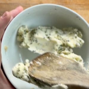 Butter with herbs being mixed in a white bowl