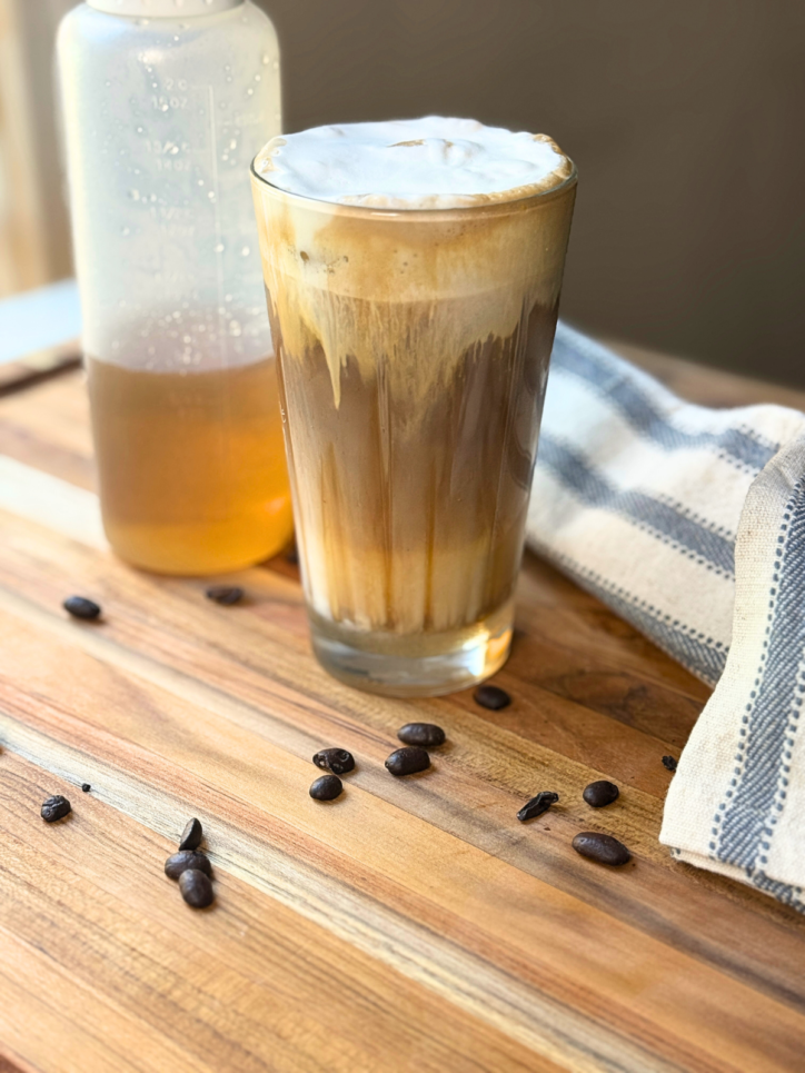 a sugar cookie latte in a glass, with  syrup behind it in a squeeze bottle