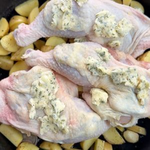 Chicken legs with compound butter on top of potatoes in a cast iron skillet