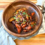 glazed carrots in a wooden bowl, with a pewter plate underneath