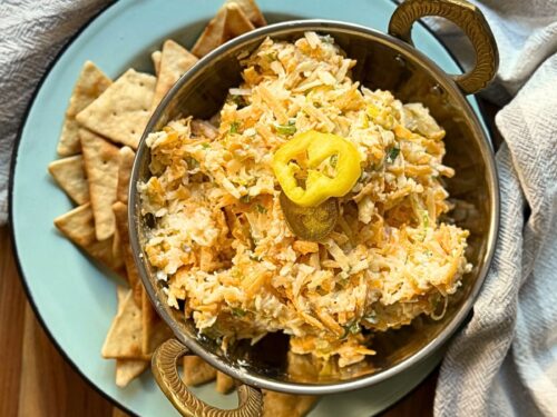 cheese spread in a silver bowl on a blue plate with pita chips around the bottom