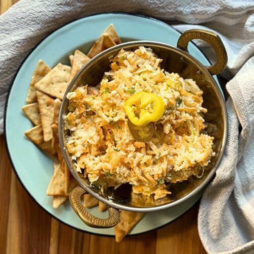 cheese spread in a silver bowl on a blue plate with pita chips around the bottom