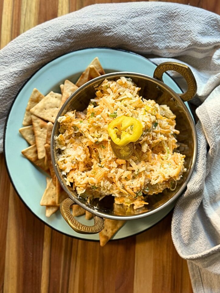 cheese spread in a silver bowl on a blue plate with pita chips around the bottom