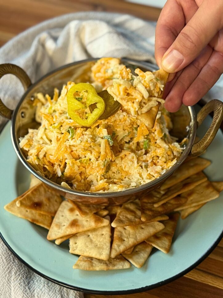 hand holding a pita chip with spicy cheese spread on the chip