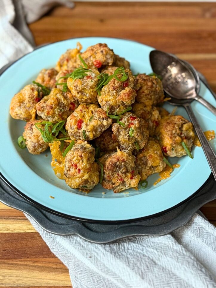 Sausage balls piled on a light blue plate with a spoon and green onions on top