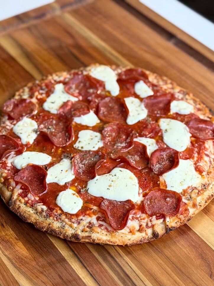 A whole freshly baked pizza with fresh mozzarella on a cutting board