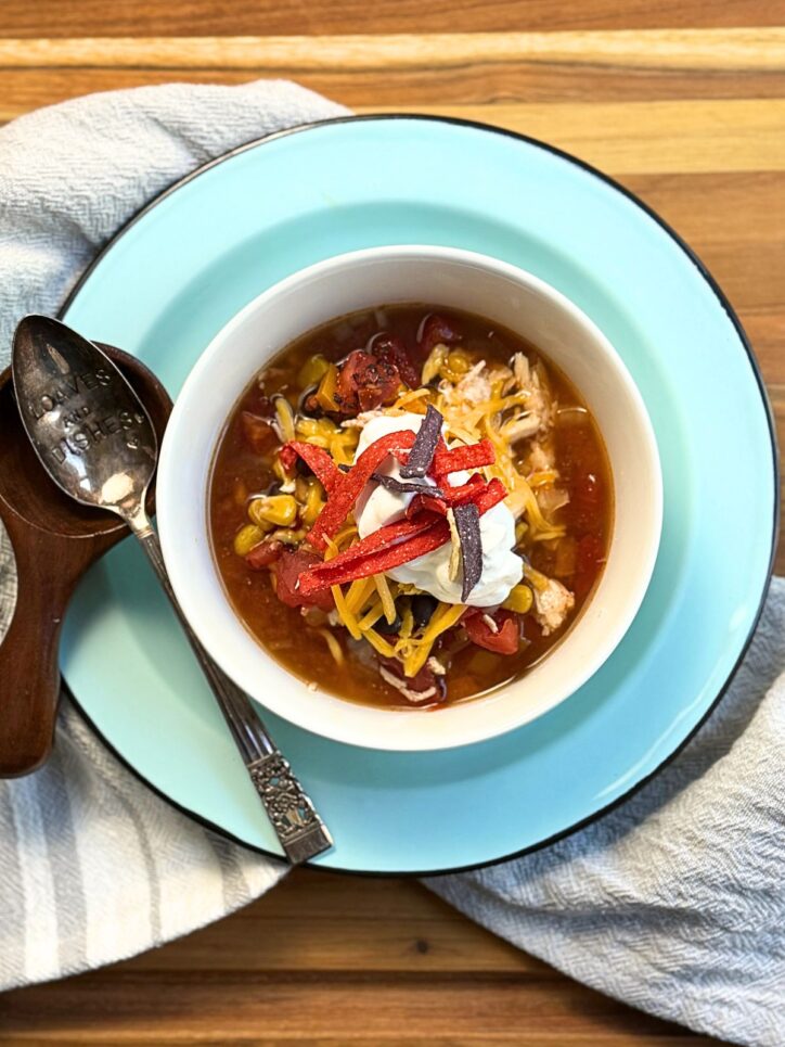 Bowl of Chicken Tortilla Soup garnished with tortilla strips and sour cream on a turquoise plate