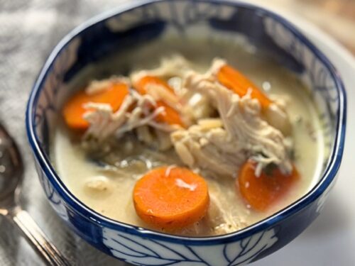 Close-up of chicken soup showing perfectly sliced carrots and tender shredded chicken in a creamy broth, served in a decorative blue-rimmed bowl