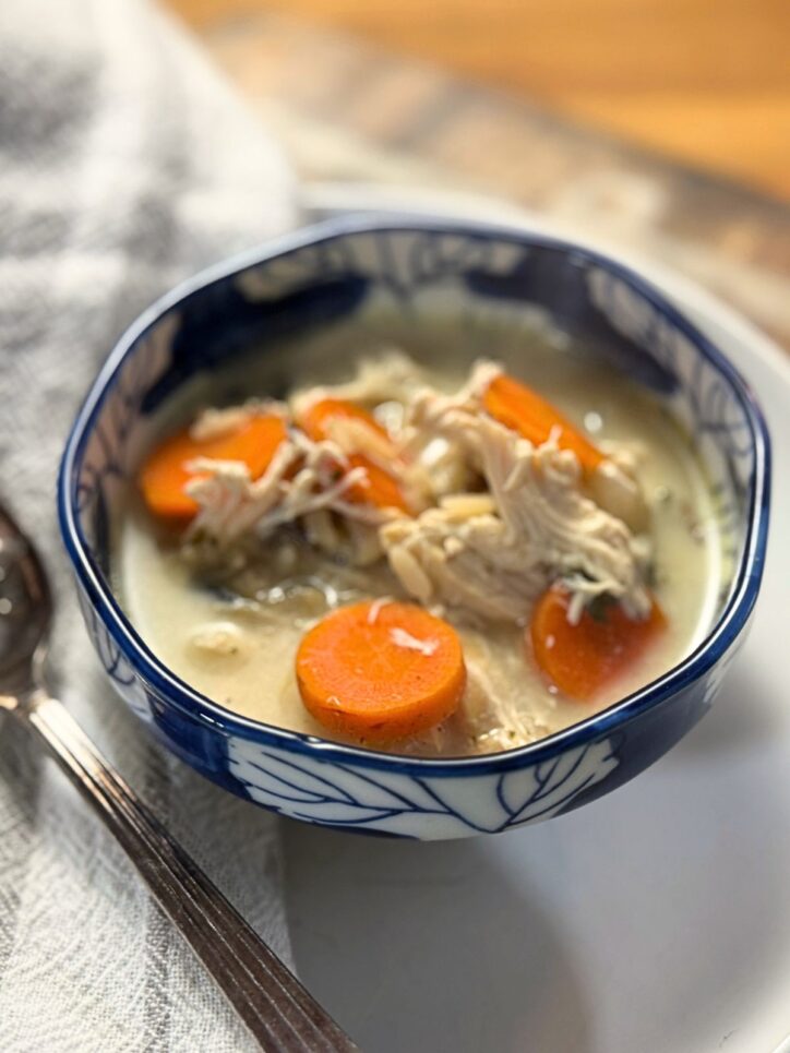 Close-up of chicken soup showing perfectly sliced carrots and tender shredded chicken in a creamy broth, served in a decorative blue-rimmed bowl