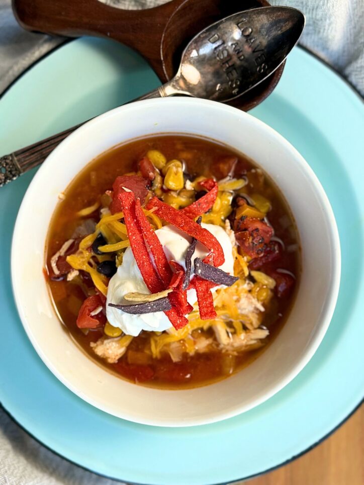 Soup in a white bowl, with sour cream, and tortilla strips on top.