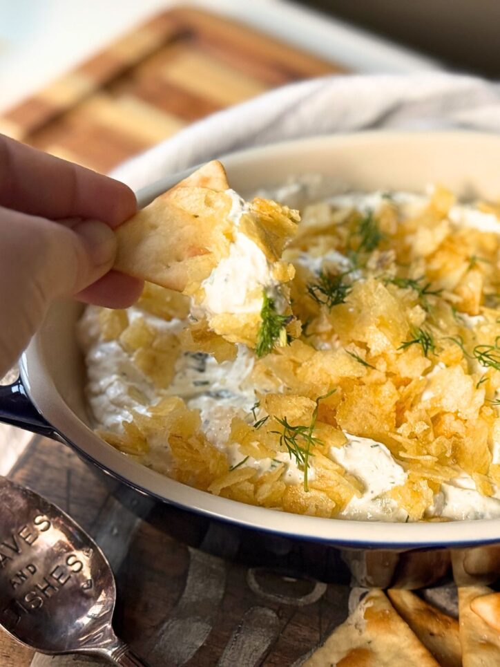 hand holding a pita chip, scooping up some of the dill pickle dip.