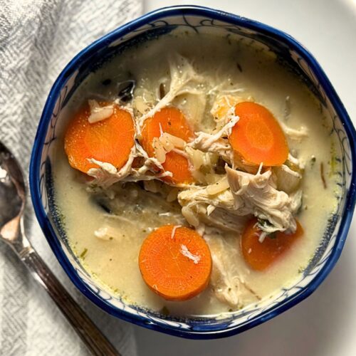 Overhead view of chicken soup with vibrant orange carrot rounds and pulled chicken pieces floating in a light-colored broth, served in an Asian-inspired blue and white bowl