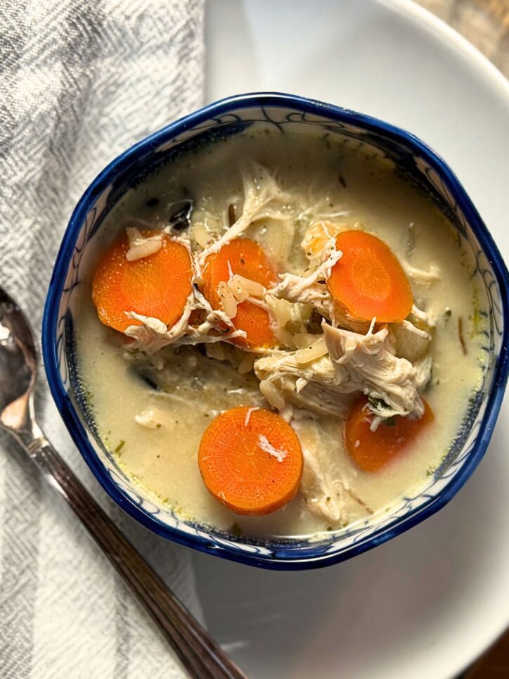 Overhead view of chicken soup with vibrant orange carrot rounds and pulled chicken pieces floating in a light-colored broth, served in an Asian-inspired blue and white bowl