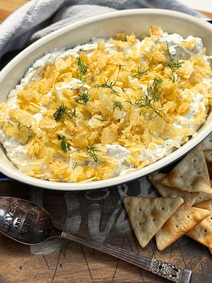 Dill pickle dip in a cassrole dish with pita chips on the side.