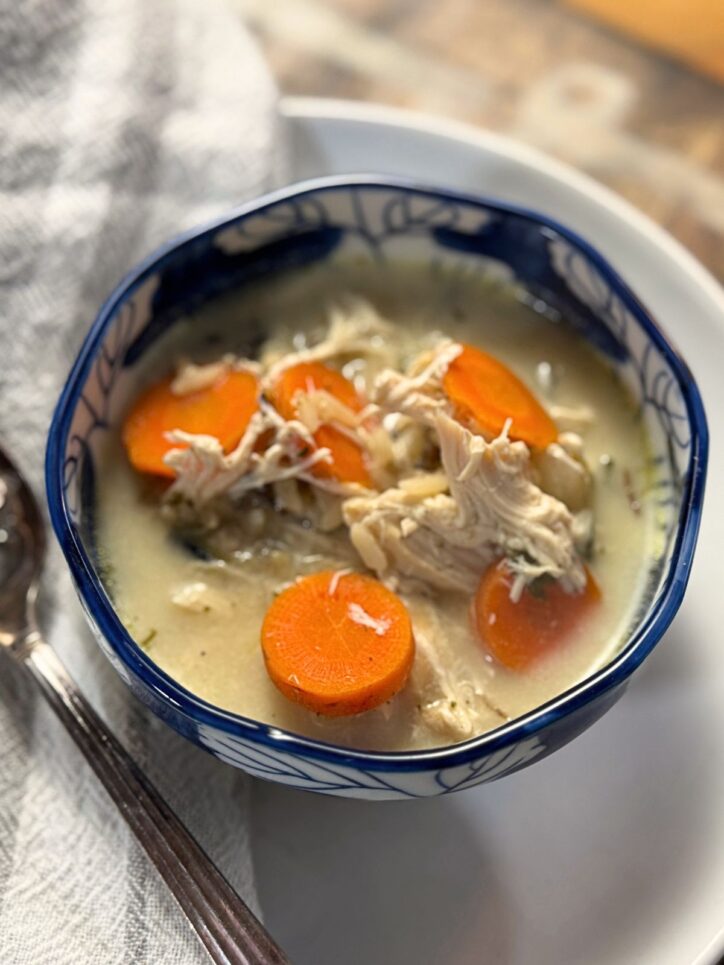 Angled view of creamy chicken soup showing the depth of the bowl and the layering of ingredients, with carrots and chicken in a pale broth