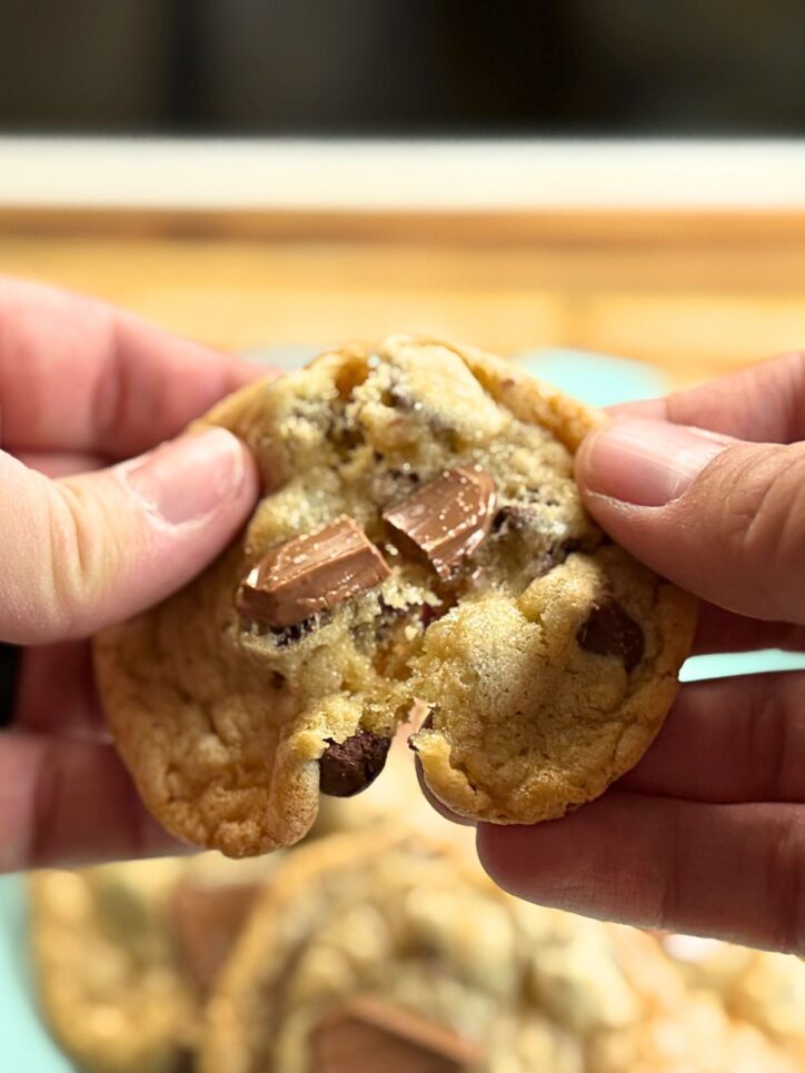 Hands breaking open a chocolate chip cookie, showing melted chocolate and soft texture