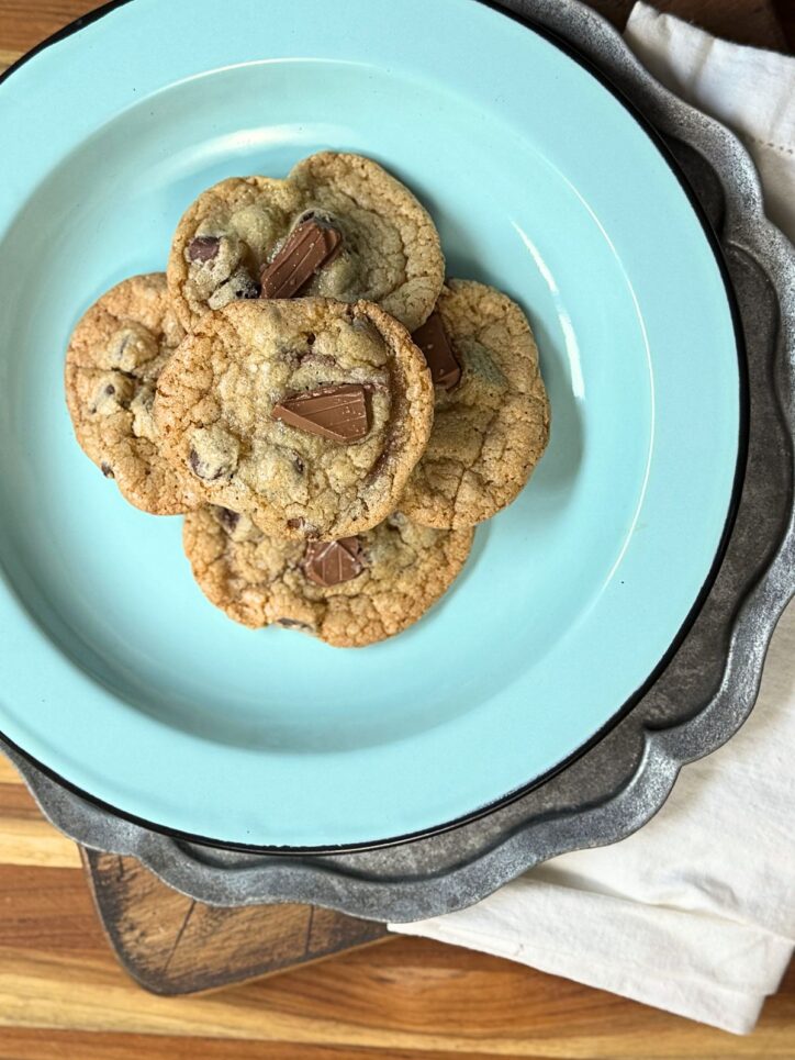 Four chocolate chip cookies on a turquoise plate set on a decorative metal tray with white napkin