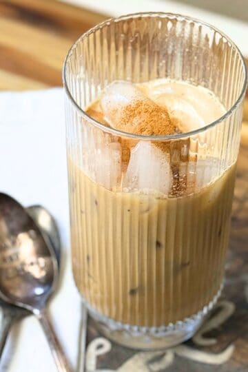 Glass of Vietnamese iced coffee with ice cubes and a sprinkle of cinnamon on top, served in a ribbed glass with a spoon beside it.