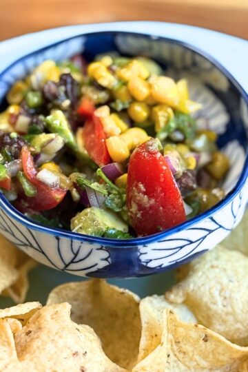 cowboy caviar in a blue and white bowl with tortilla chips on a blue plate