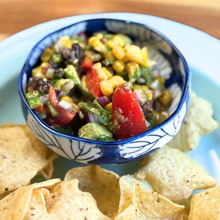 cowboy caviar in a blue and white bowl with tortilla chips on a blue plate