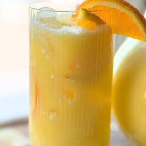 Close-up of an Orange Coconut Refresher in a tall ribbed glass with orange slice garnish and ice cubes.