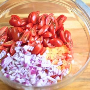 Chopped onion, cherry tomato, and bell peppers in a glass bowl